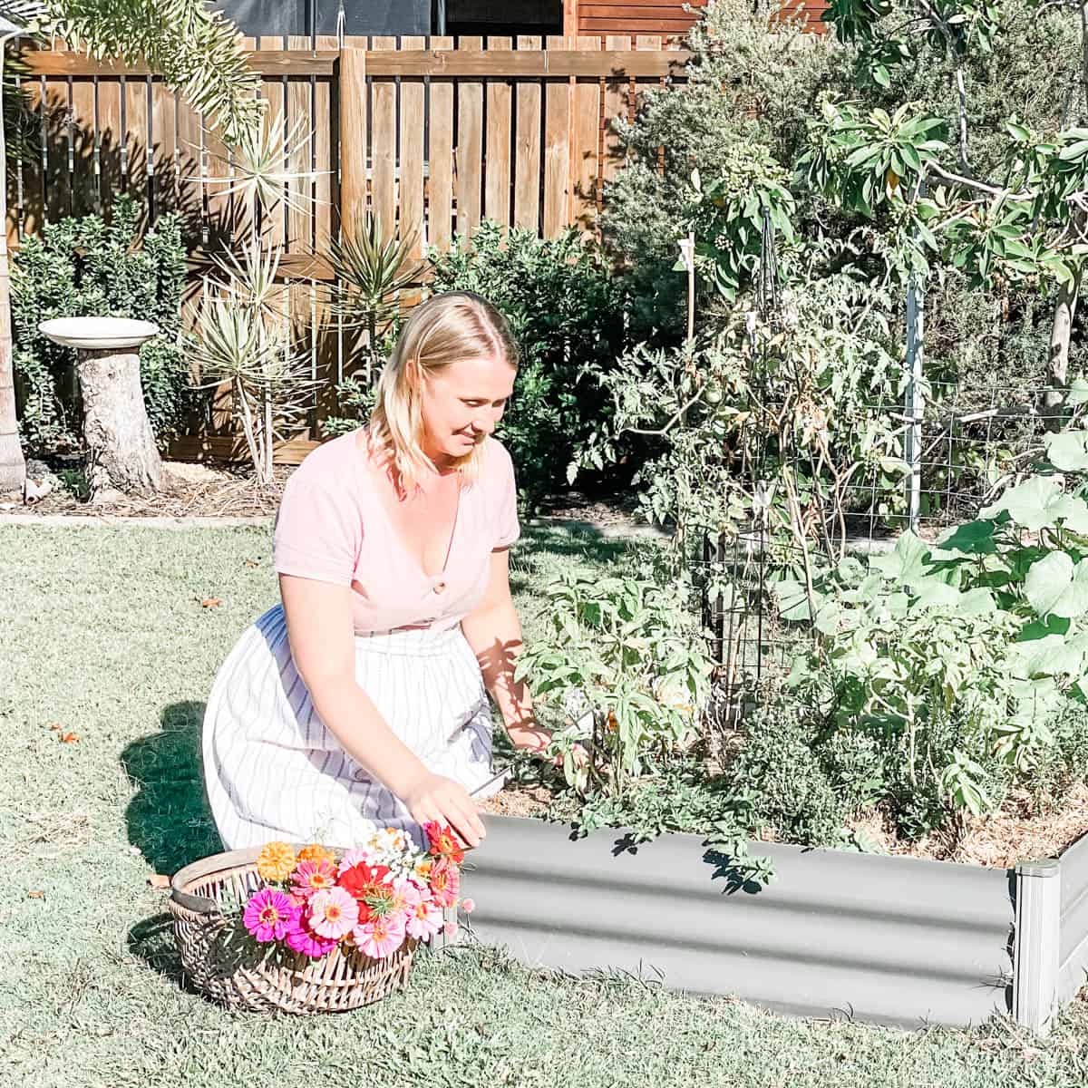 Photo of Emily kneeling by a raised garden bed next to a basket of flowers