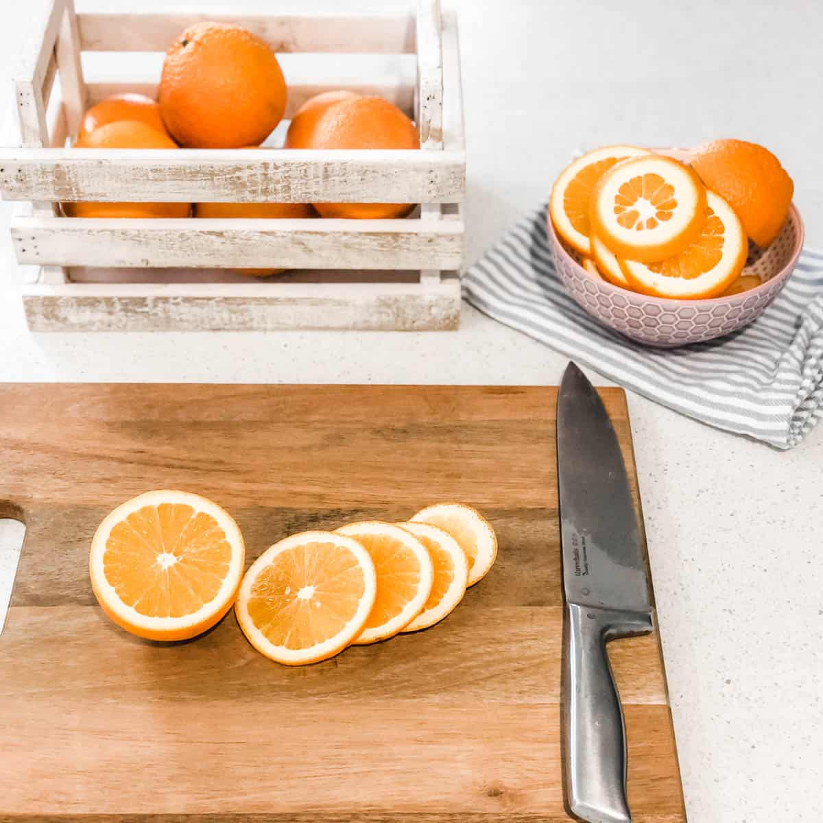 Picture of a small crate on organise on a kitchen bench with a wooden chopping board, knife and a bowl of slices oranges