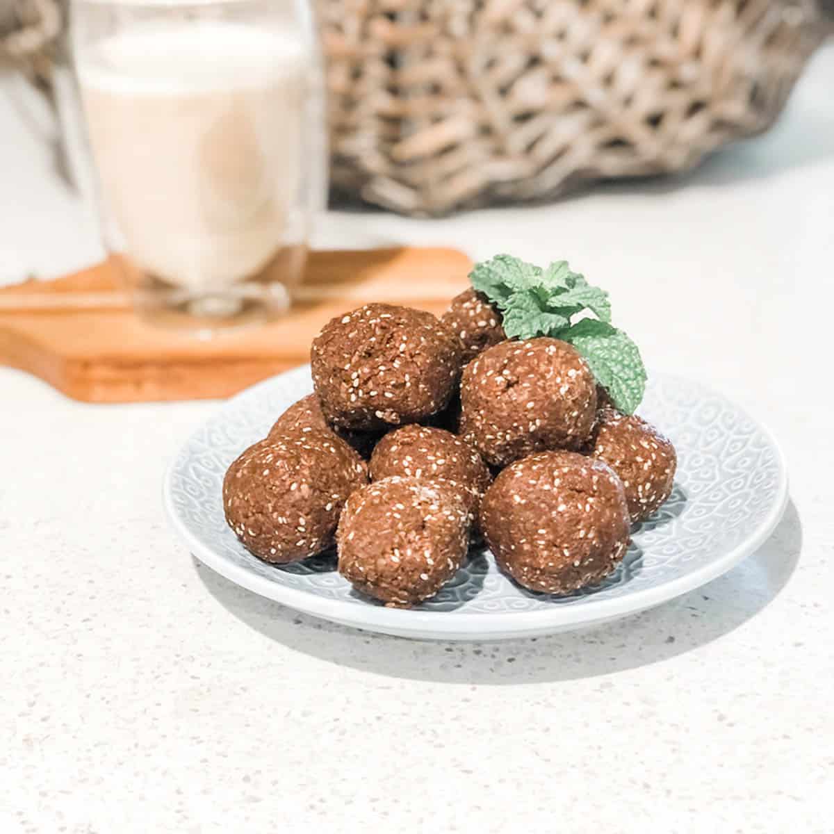 photo of pile of chocolate bliss balls on a blue plate with a cup of coffee in the background