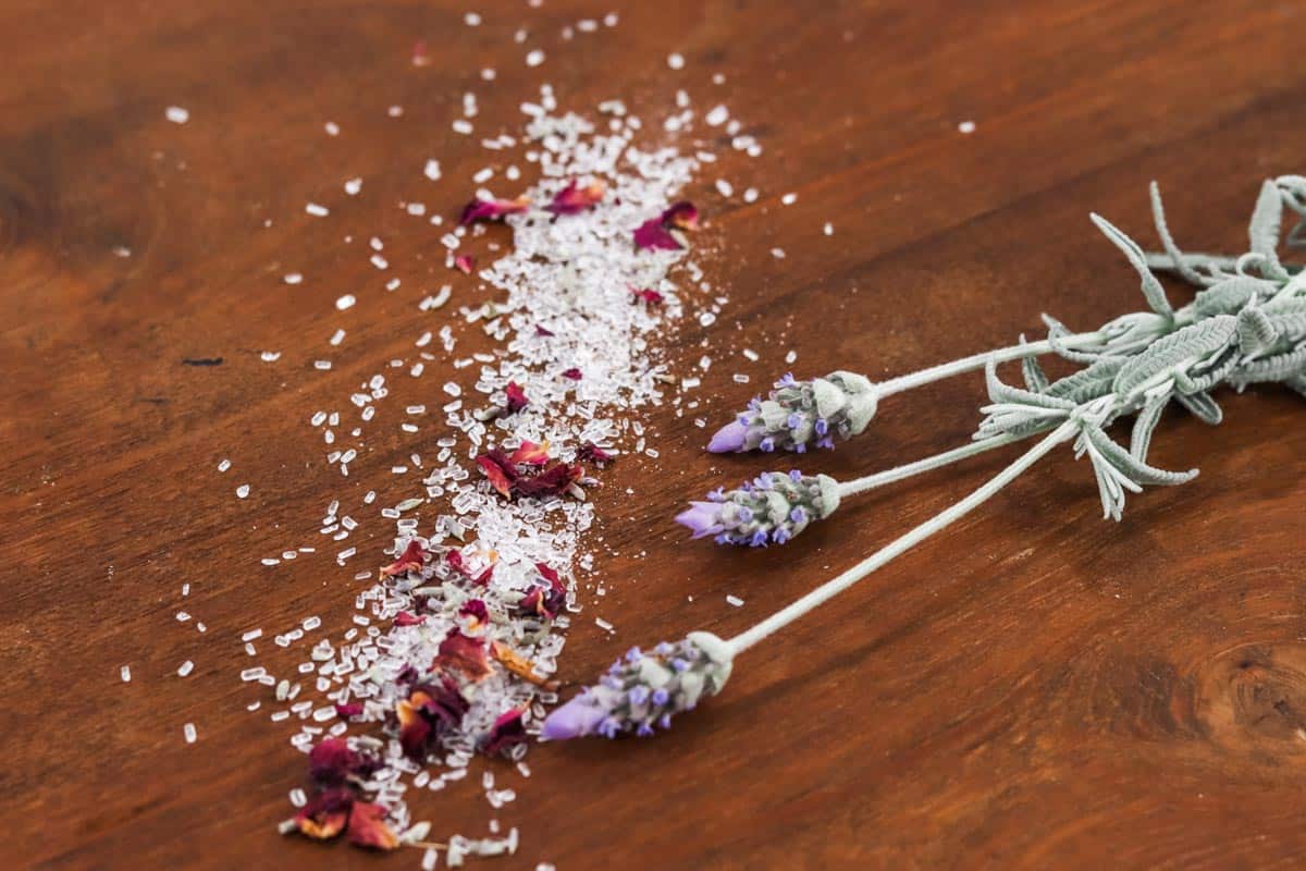 Image of bath salts sprinkled in a line on a timber table next to three sprigs of lavender