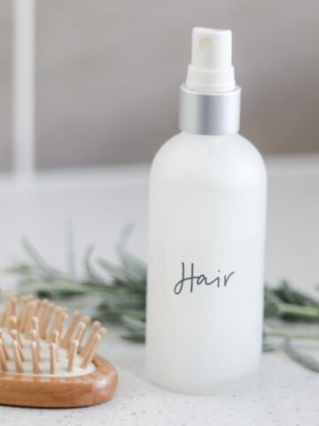 spray bottle of leave in conditioner next to a wooden hair brush and fresh lavender sprigs