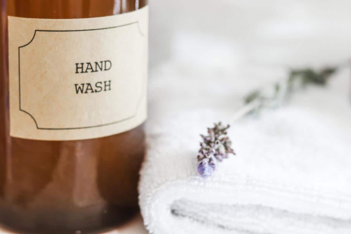 close up image of the bottom half of an amber foaming hand soap pump dispenser next to a white washcloth with a piece of lavendar