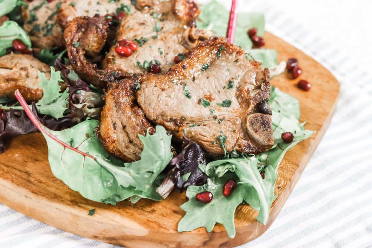 Close up image of cooked lamb chops served on a bed of mixed green salad leaves sprinkled with pomegranate seeds and finely chopped parsley