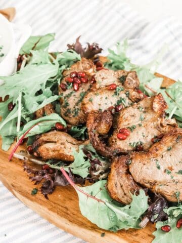Cooked lamb chops served on a bed of mixed green salad leaves sprinkled with pomegranate seeds and finely chopped parsley and a bowl of minted yogurt sauce