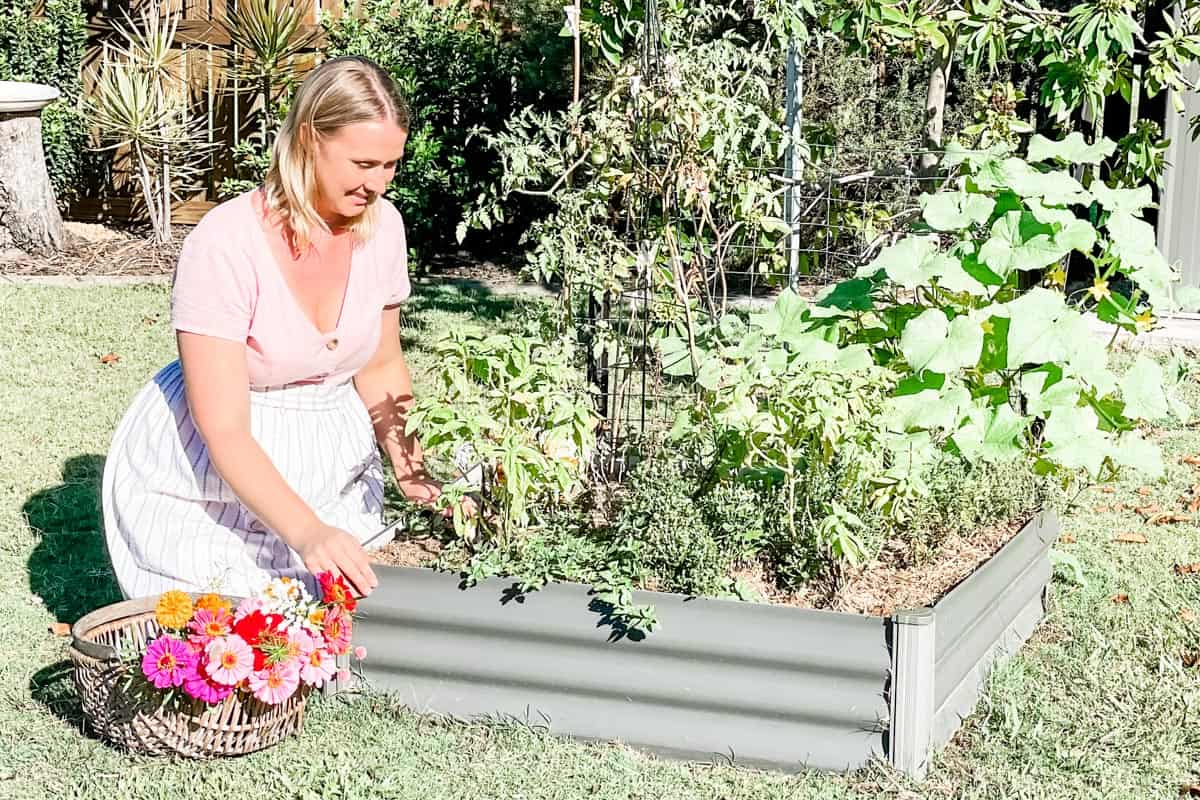 Emily kneeling next to a garden bed waring an apron with a basket of flowers