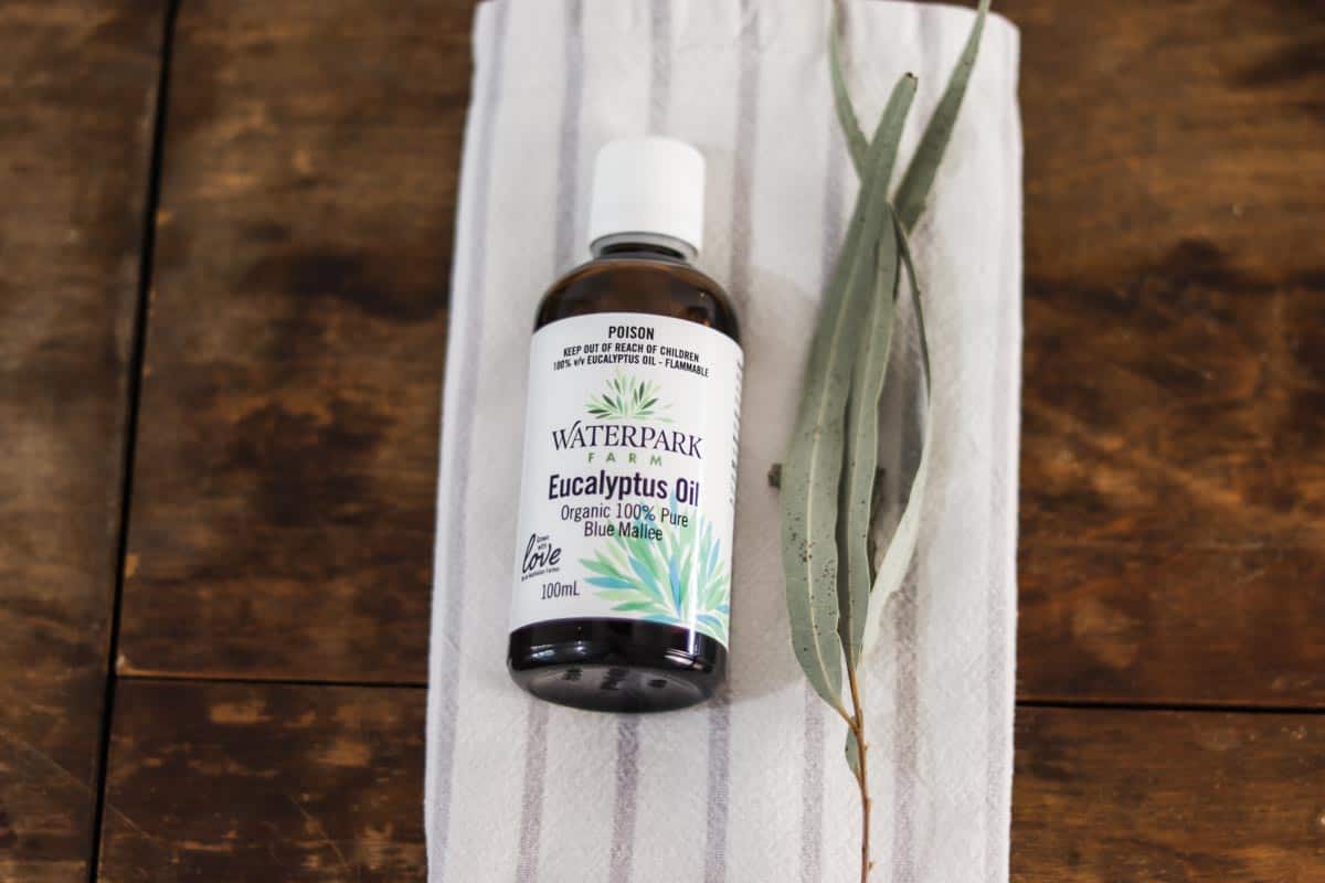 Image of a bottle of waterpark farm eucalyptus oil laid on a grey and white striped tea towel next to eucalyptus leaves