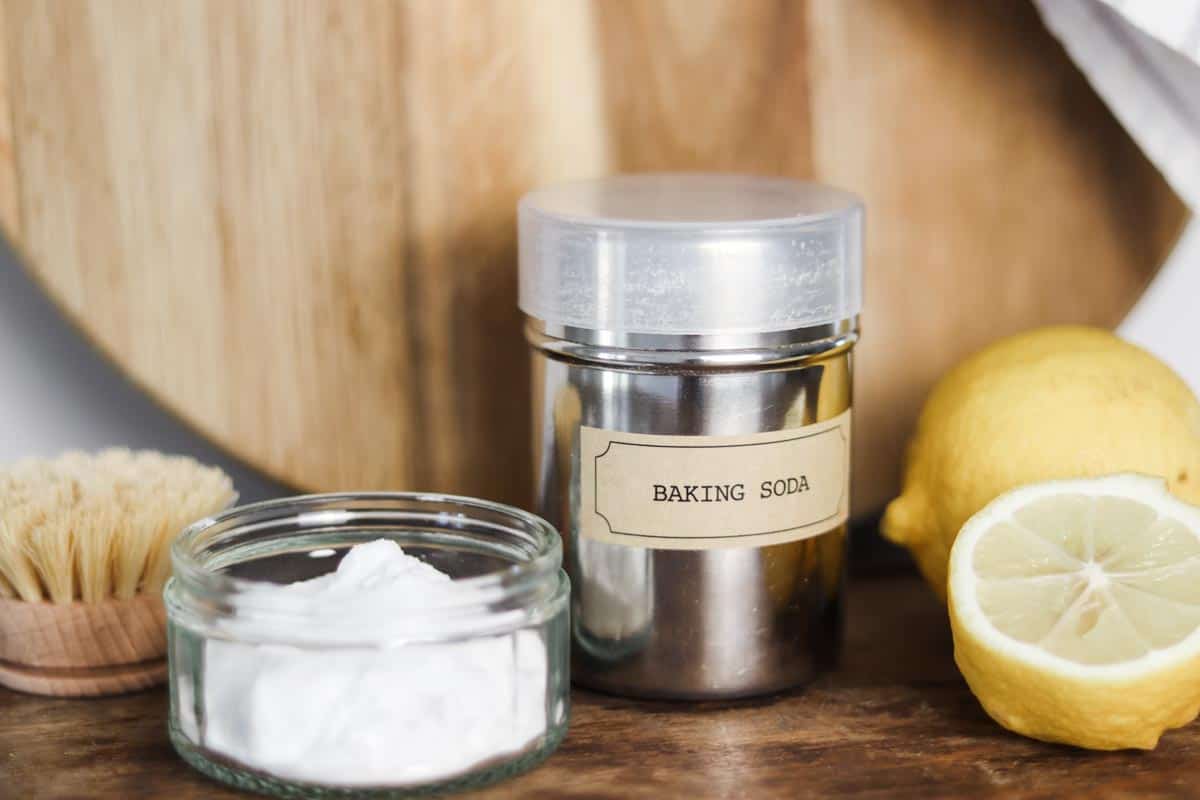 Close up image of a silver sugar shaker labeled 'baking soda' next to a glass dish of baking soda and some lemons