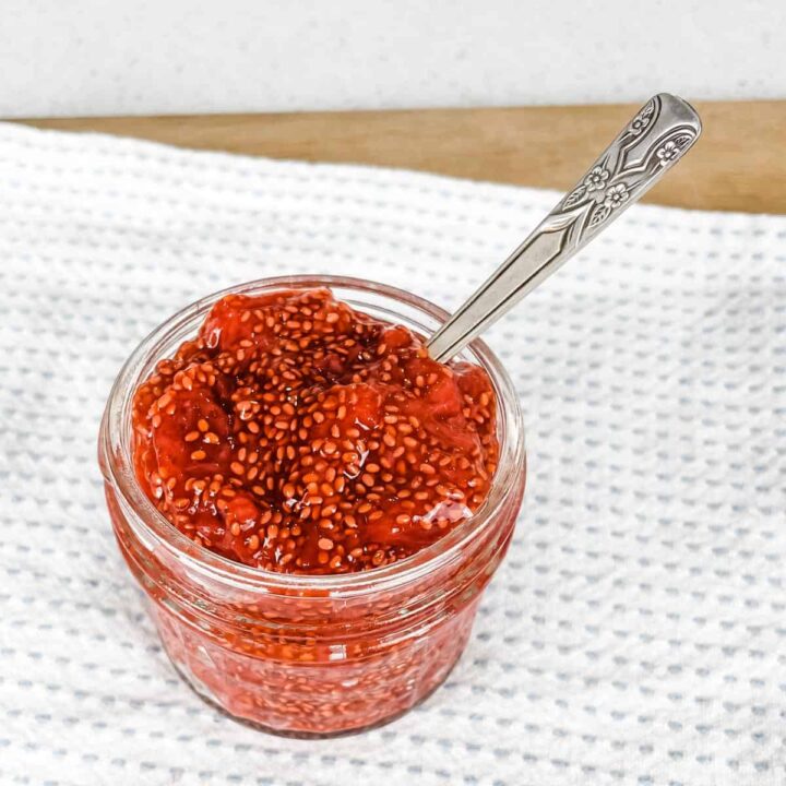 image of a glass pot of microwave strawberry chia jam with a spoon in it