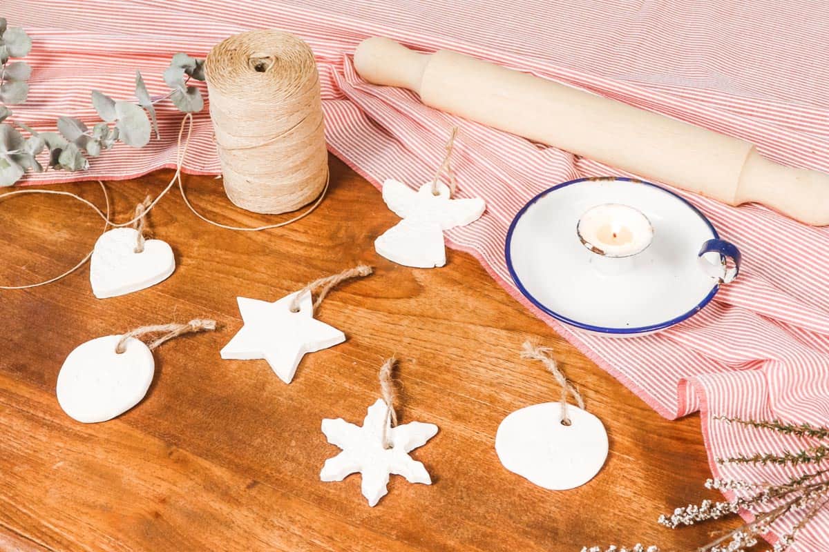 Image of ornaments laid out on a wooden table with a red and white striped table cloth next to a rolling pin twine and a candle