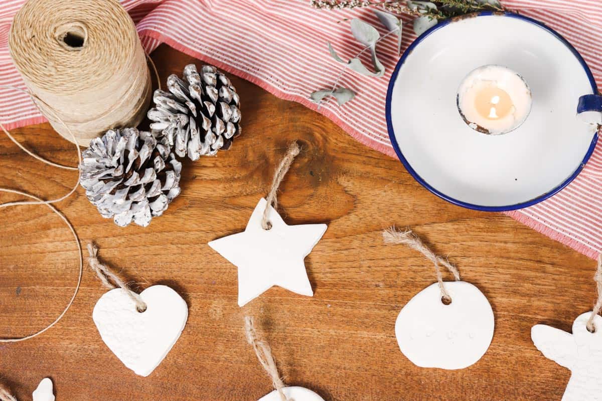 Image of ornaments laid out on a wooden table with a red and white striped table cloth next to two pine cones twine and a candle