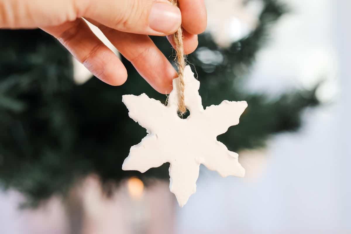 Close up image of a hand holding a snowflake shape ornament with Christmas tree in the background
