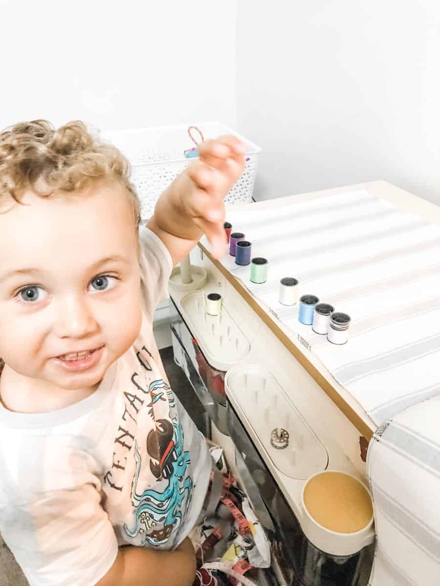 William at home sewing. William is helping by organising spools of cotton on the sewing desk