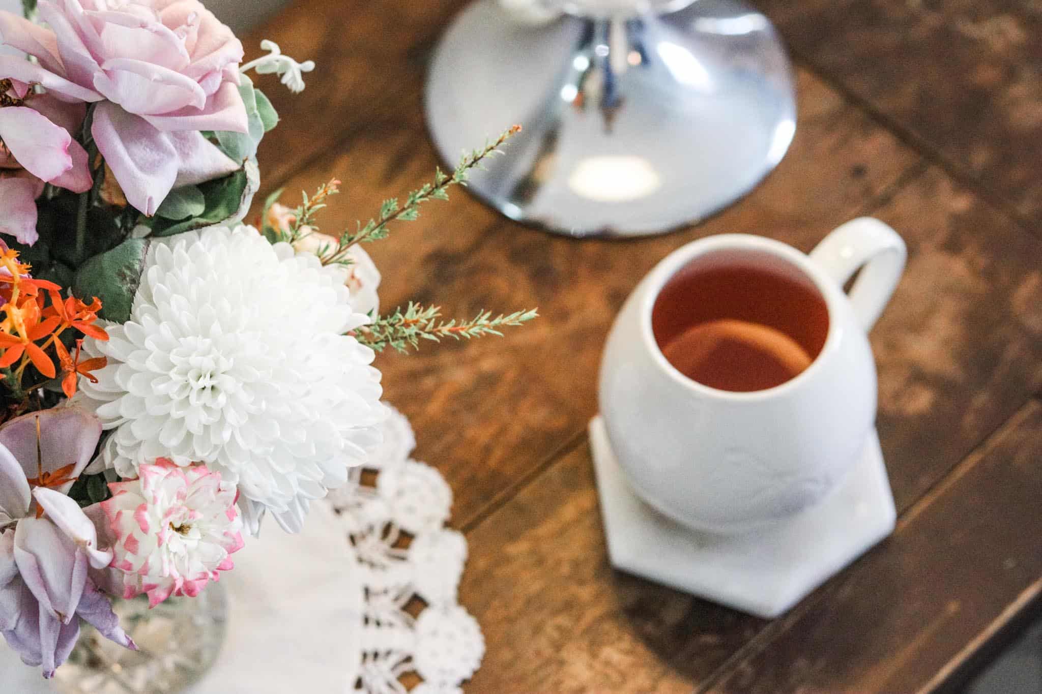Overhead image of a cup of tea set on a table upon a marble coaster next to a vase of flowers