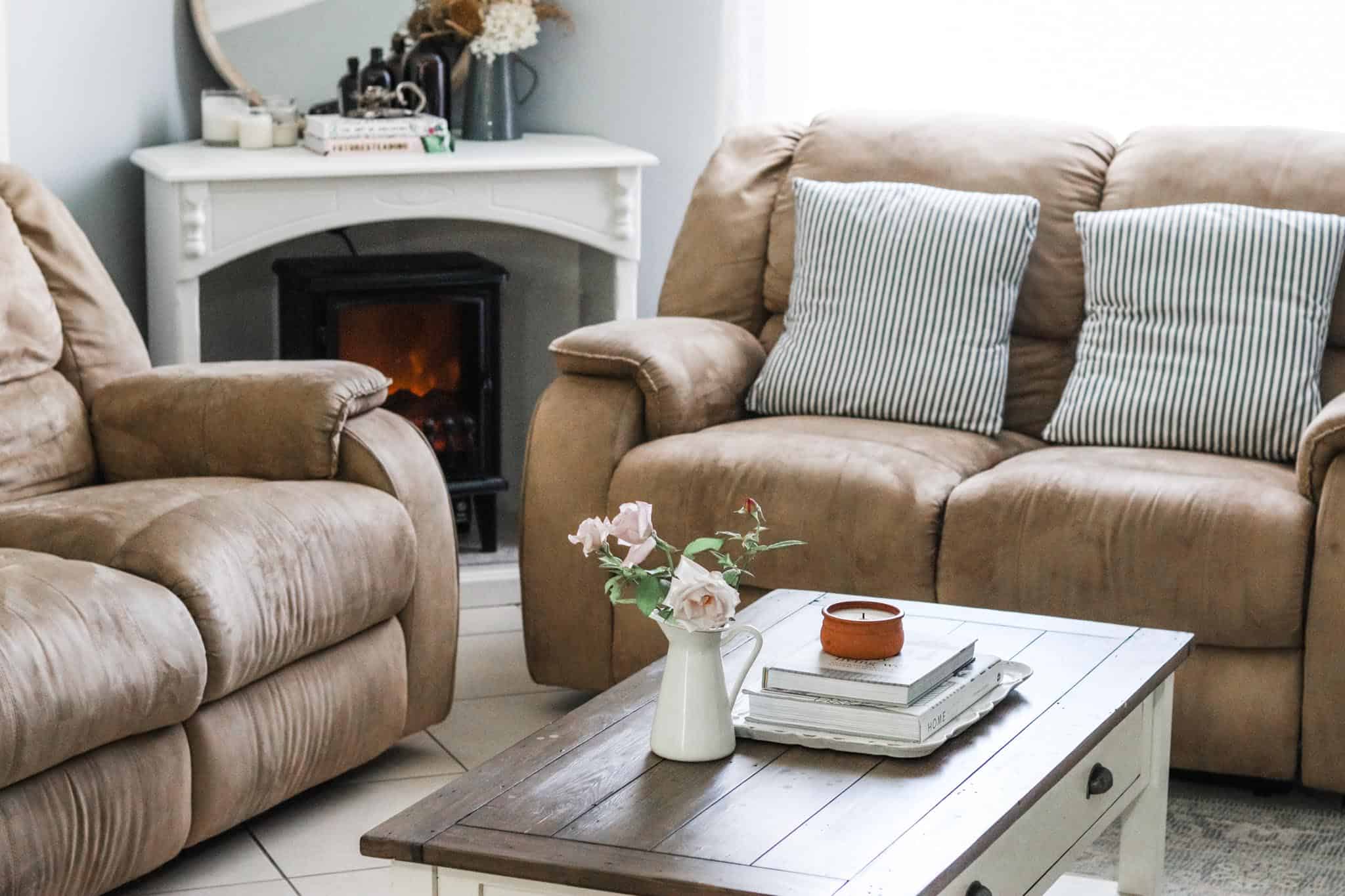 Image of neat and tidy living room with coffee table, books, candle, vase of roses, cushions, fireplace