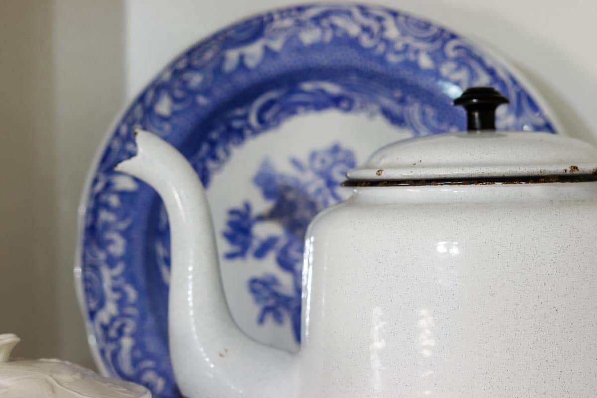 Close up image of a chippy blue grey enamel teapot with a blue and white decorative plate behind it