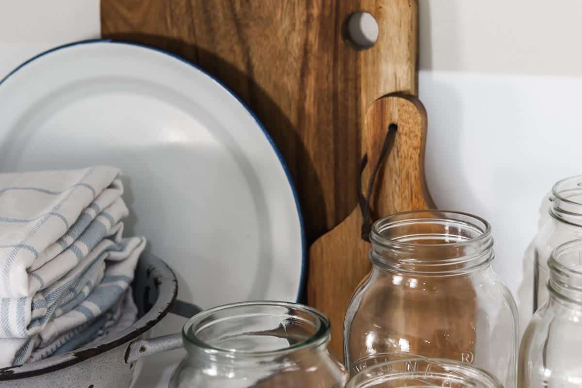 Close up image of the tops of some empty jars, serving boards, enamel kitchenware and tea towels on a shelf