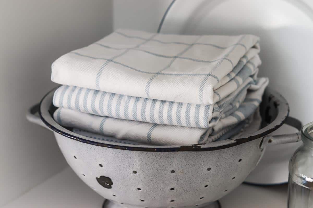 Close up image of a vintage chippy blue grey colander filled with folded blue and white tea towels