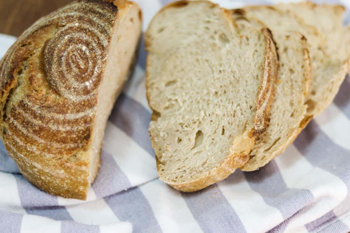 Image of a loaf of sourdough bread, sliced, sitting on top of a blue and white tea towel