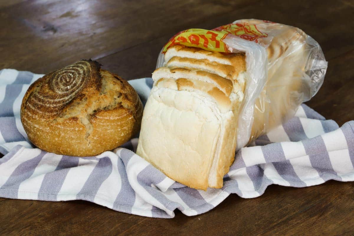 A loaf of sourdough bread next to a loaf of white sliced conventional bread to show what makes sourdough bread different