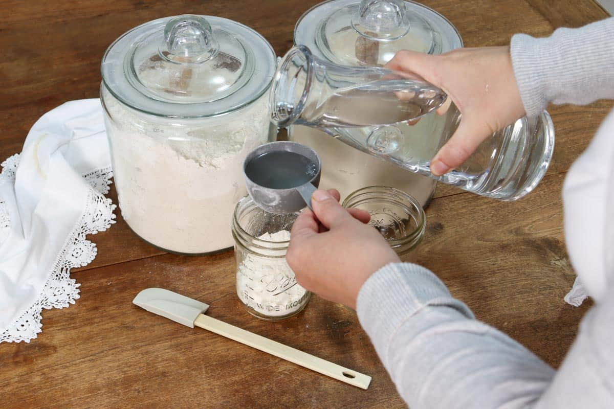 Adding a half a cup of water to a glass mason jar to make sourdough starter