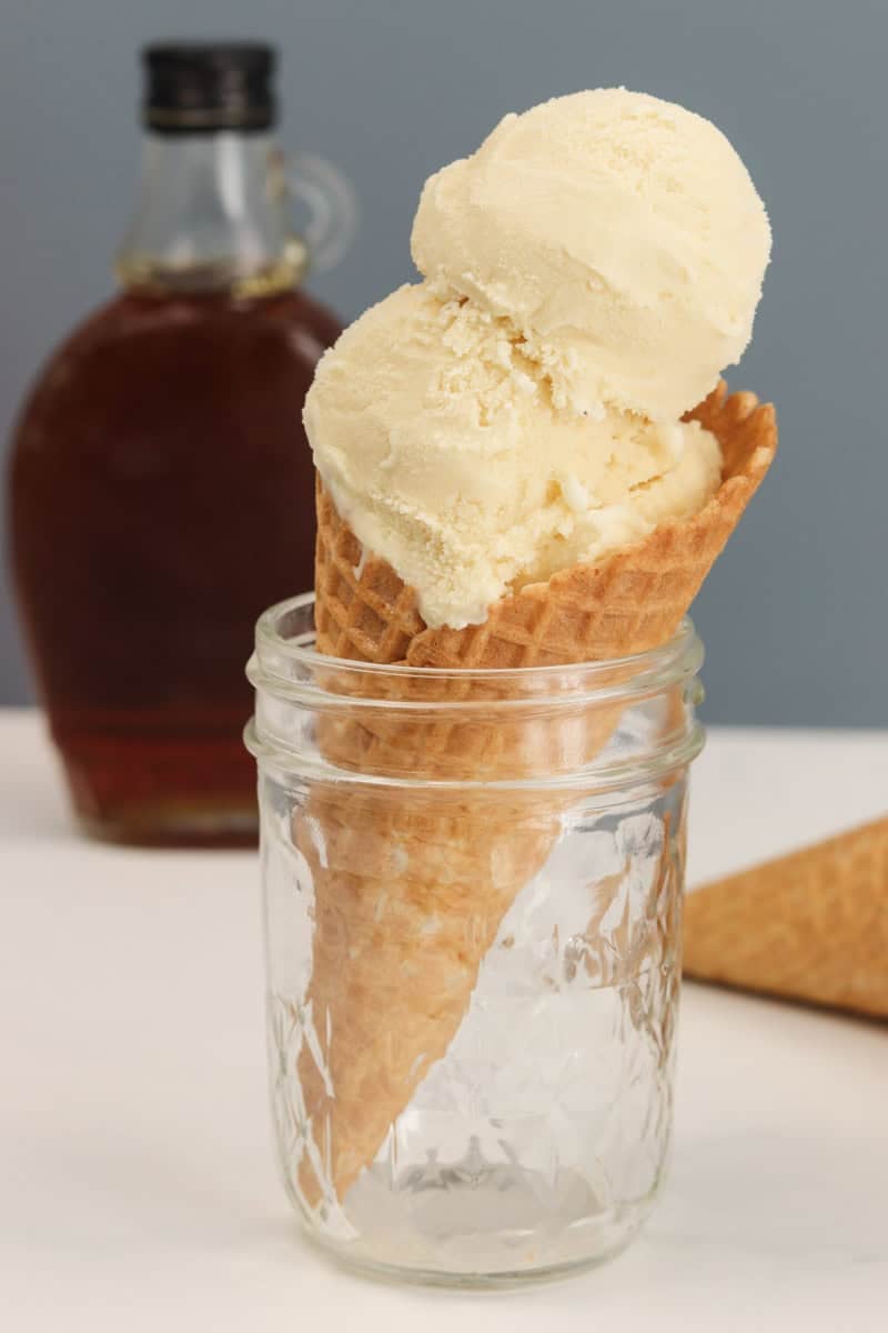 an ice cream cone standing in a jar in front of a bottle of maple syrup