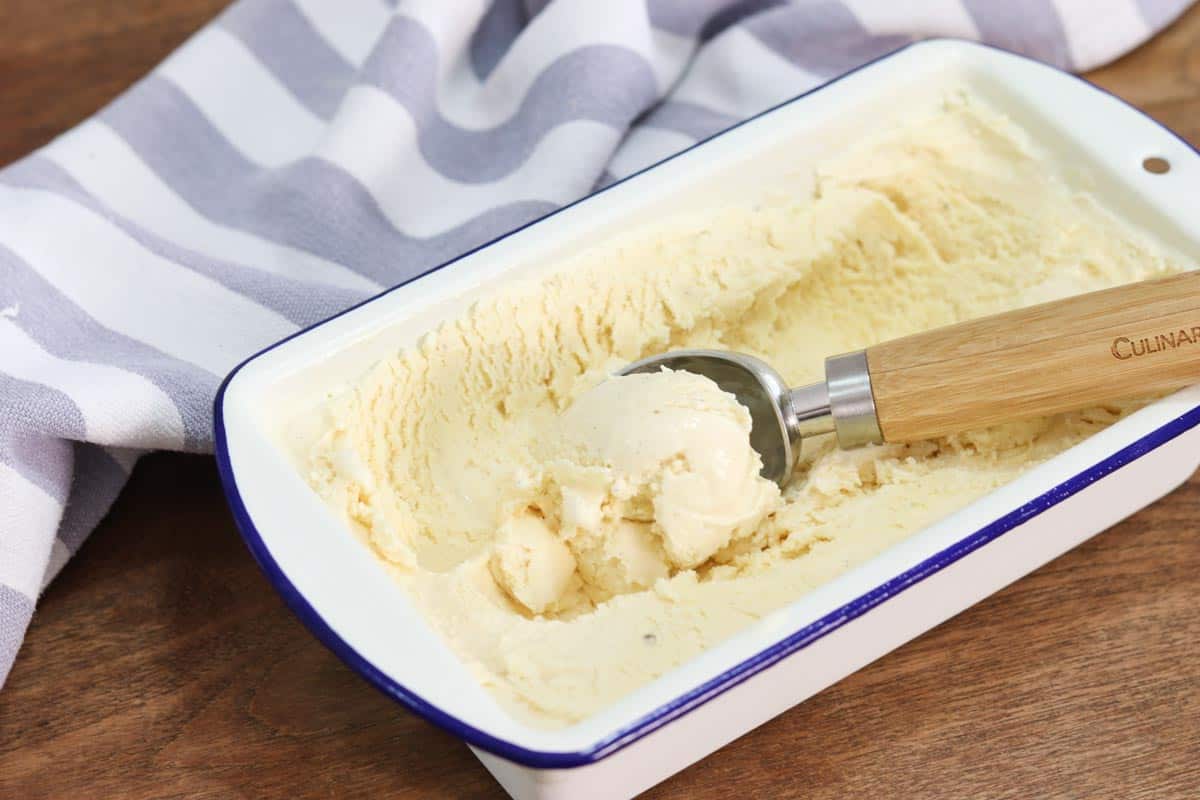 A load tin filled with vanilla ice cream and an ice cream scoop sitting on top
