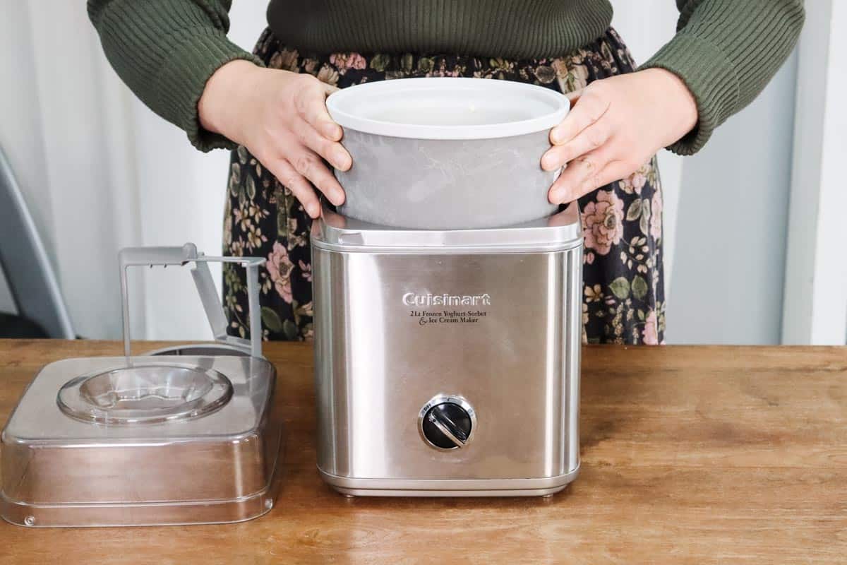 The frozen ice cream maker insert filled with the vanilla ice cream mixture with eggs is being inserted into the ice cream maker