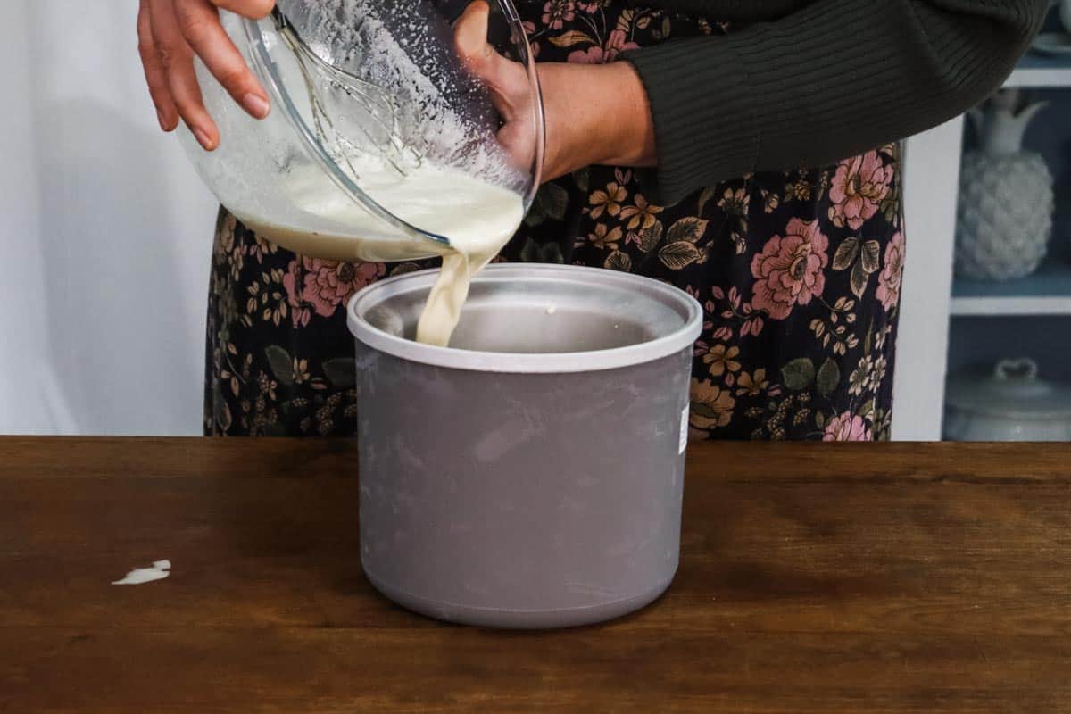 The ice cream mixture is being poured from a glass mixing bowl into the frozen ice cream maker insert