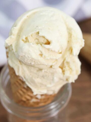 A close up image of a waffle ice cream cone filled with vanilla ice cream sitting in a glass mason jar