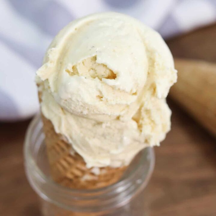 A close up image of a waffle ice cream cone filled with vanilla ice cream sitting in a glass mason jar
