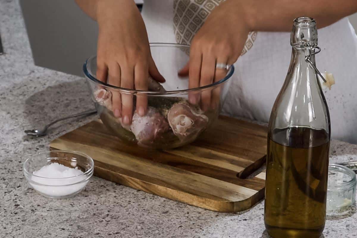 Mixing the chicken drumsticks and marinade ingredients together by hand in a glass bowl