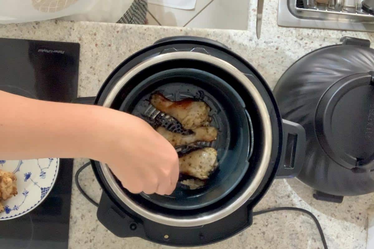 Taking the semi cooked chicken drumsticks out of the aibfryer unit and placing them on a plate in order to swap the bottom pieces to the top