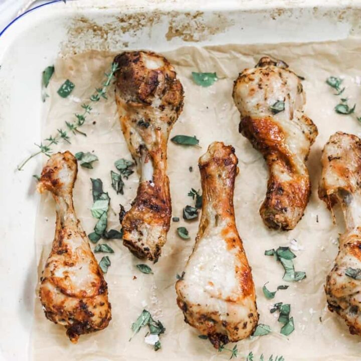 Image of cooked air fryer chicken drumsticks layed out on a tray with fresh herbs