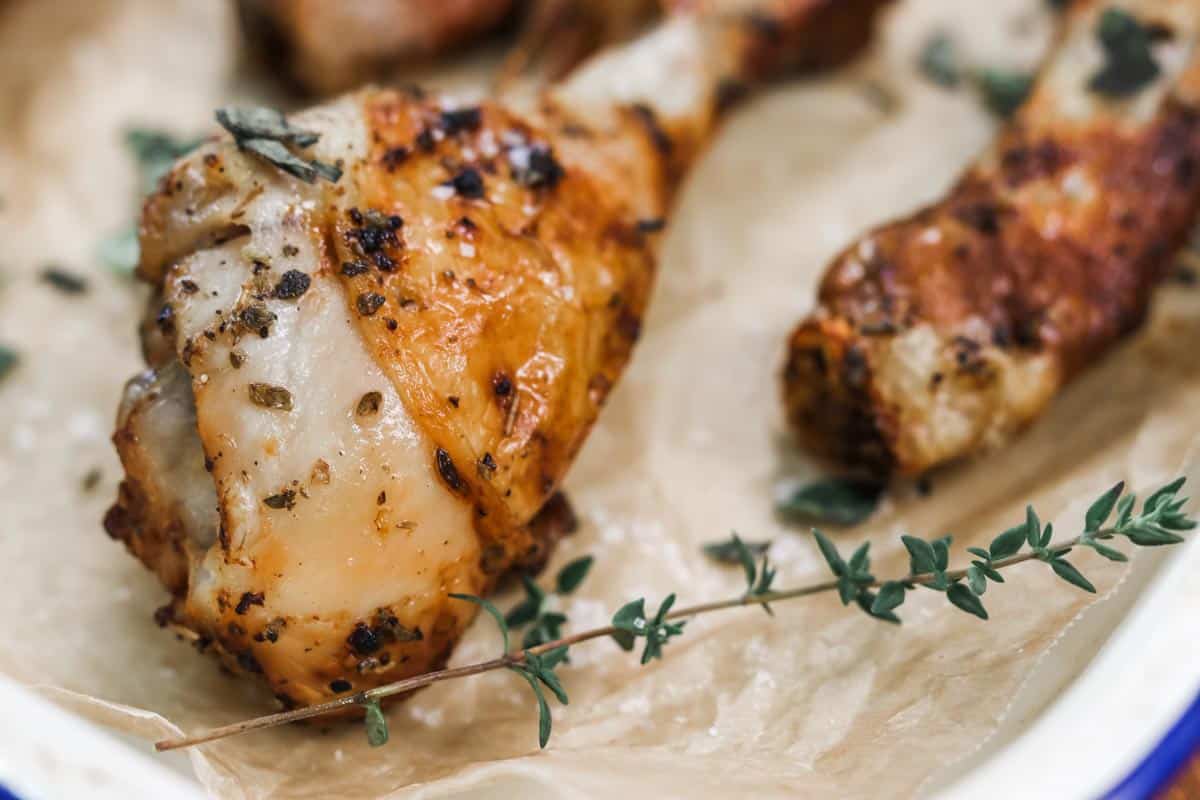 Close up image of a cooked air fryer chicken drumstick on a tray with fresh herbs