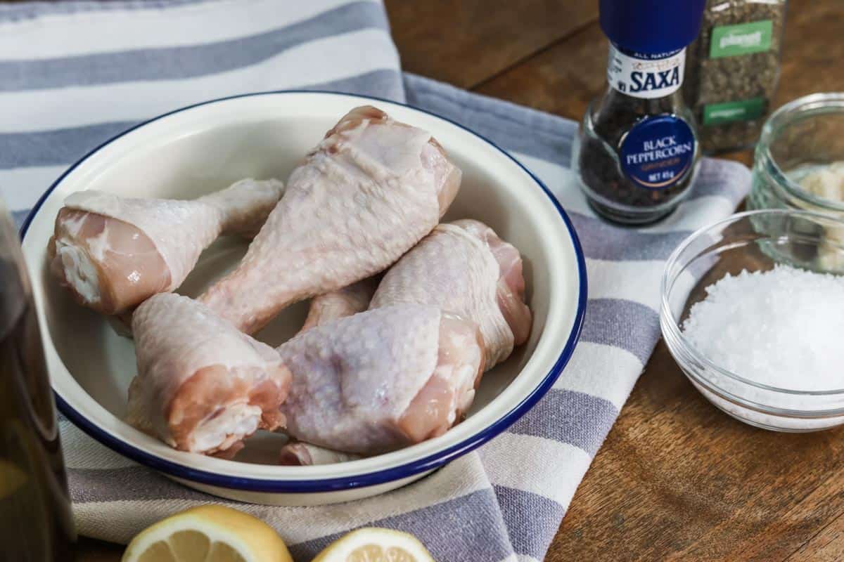 Close up image of raw chicken drumsticks in a dish next to other ingredients