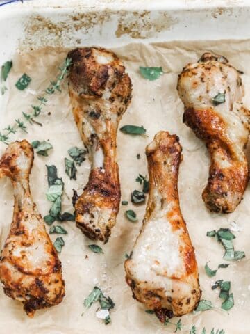 Image of cooked air fryer chicken drumsticks layed out on a tray with fresh herbs