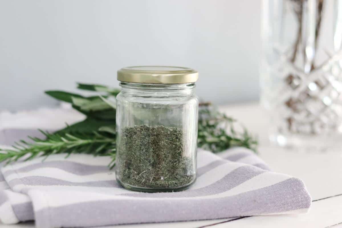 dried herbs in a jar in front of fresh herbs from the garden