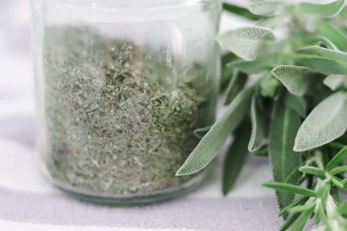 Close up image of dried herbs in a jar next to fresh herbs from the garden