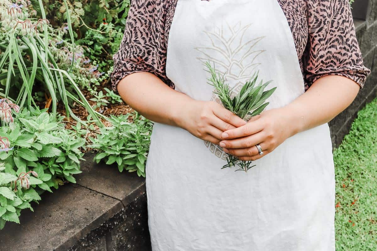 standing in the garden holding a bunch of freshly pickers herbs