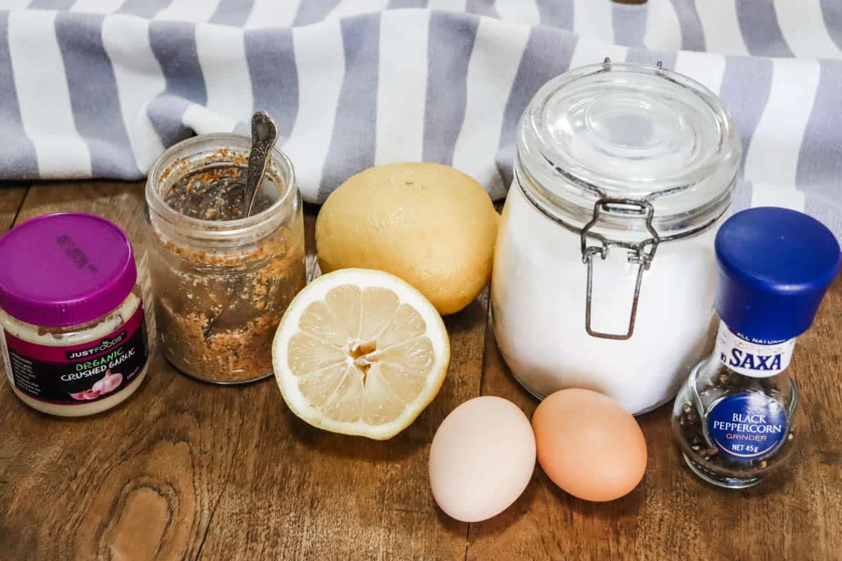 A group of ingredients to make homemade mayonnaise including garlic, mustard, lemon, eggs, salt and pepper