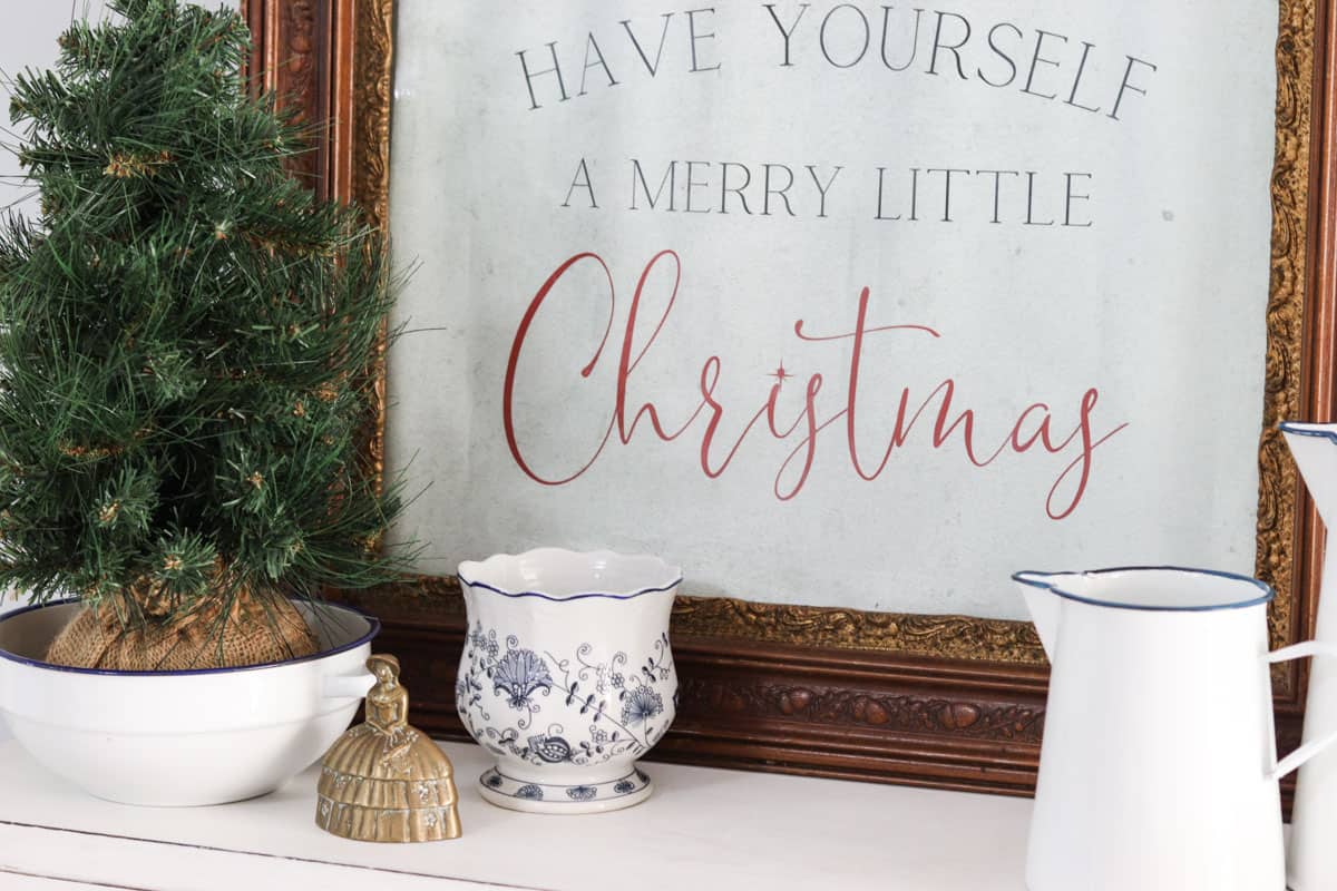 A vintage style poster reads "have yourself a merry little Christmas" in a vintage frame, set next to cottage style Christmas decorations