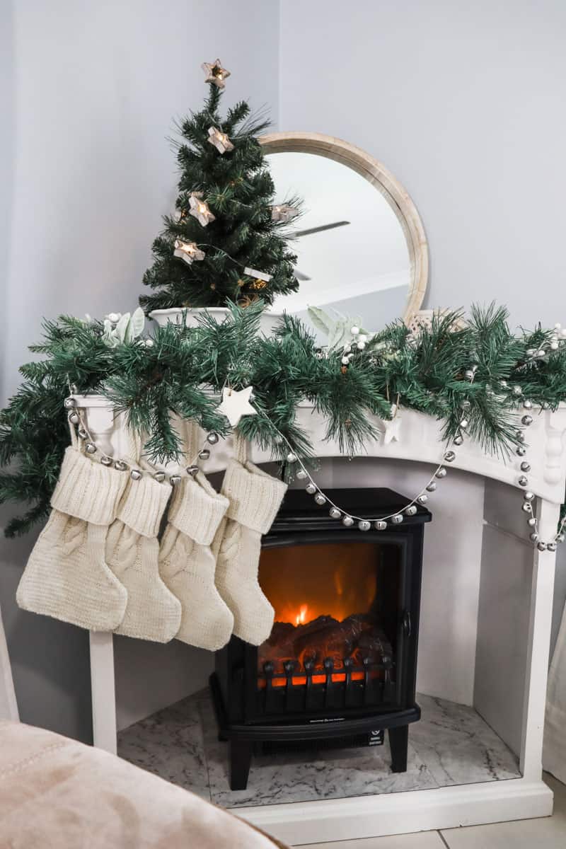 The mantle is decorated with cottage style Christmas decorations including hand knitted stockings, a thrifted bowl and small Christmas tree and silver bells