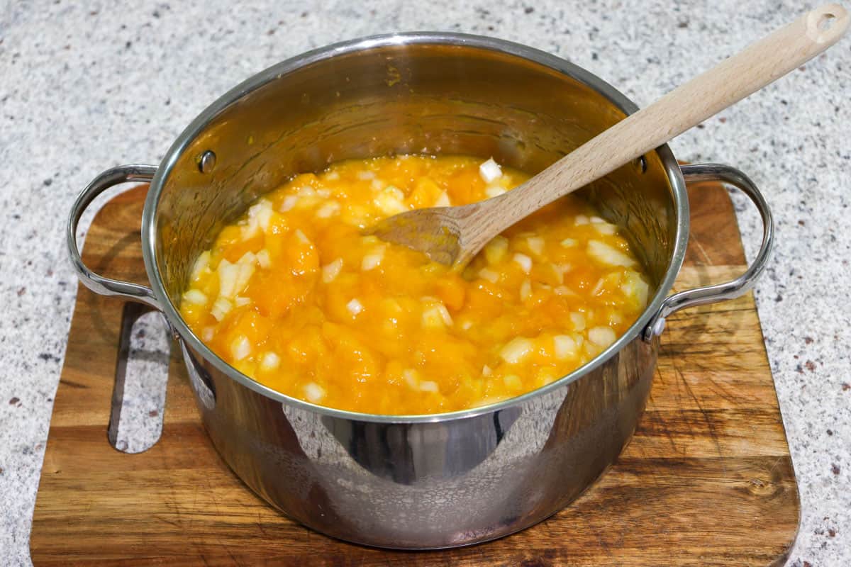 Chopped mango and onion in a large saucepan mixed with a wooden spoon