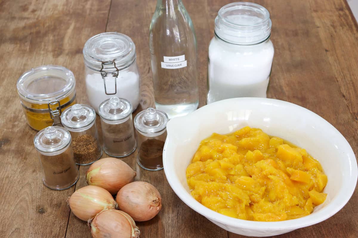 A group of ingredients used to make mango chutney including mango, onion, curry powder, salt, white vinegar, sugar and spices