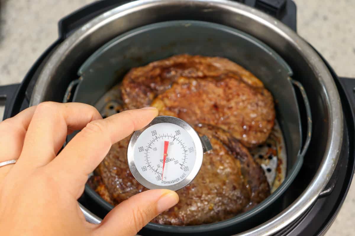 Two pieces of ribeye rib fillet steaks in an air fryer, halfway through cooking, being checked with a meat thermometer