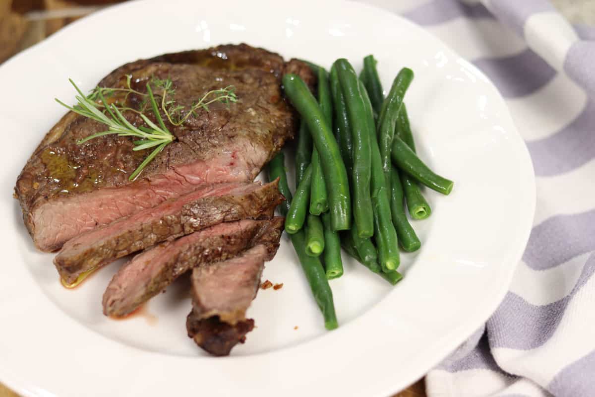 A piece of plated rib fillet ribeye steak on a plate with green beans