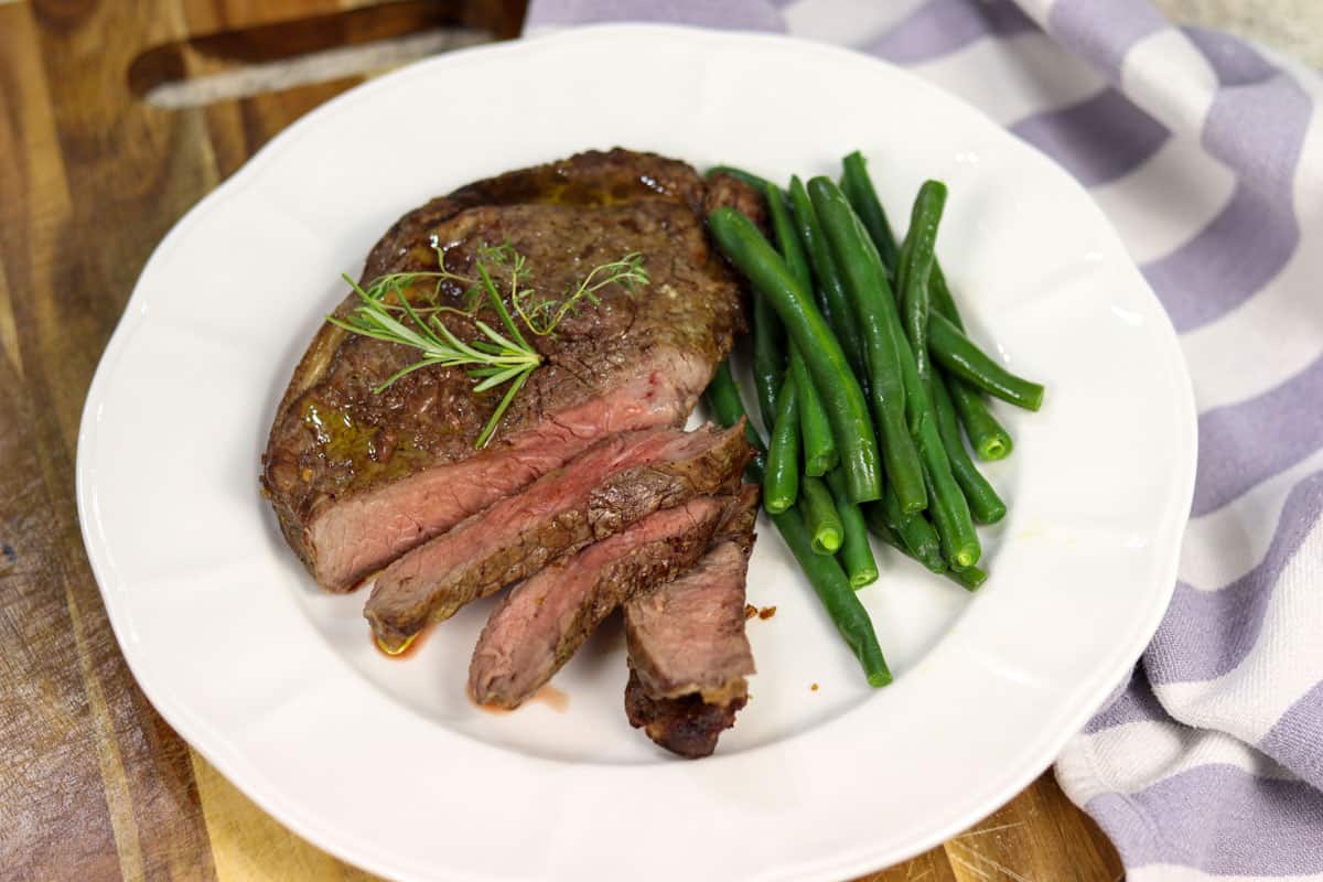 A piece of plated rib fillet ribeye steak on a plate with green beans