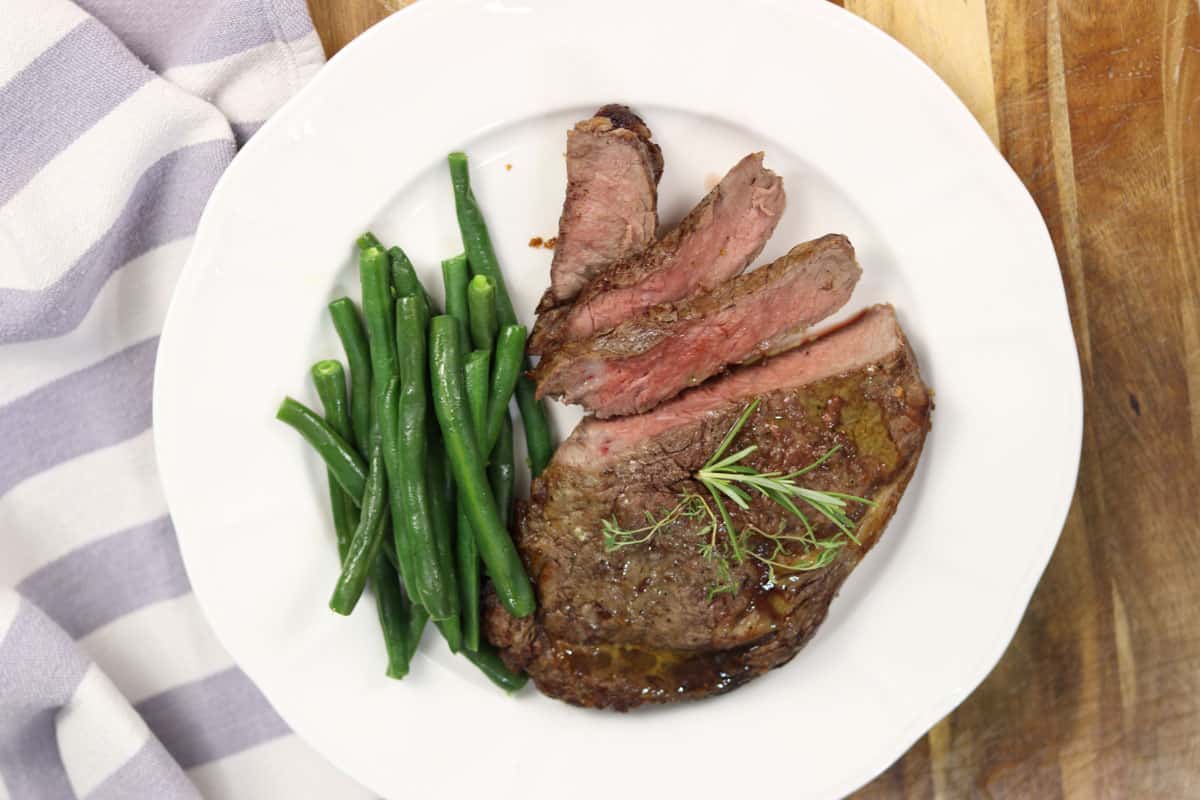 A piece of plated rib fillet ribeye steak on a plate with green beans