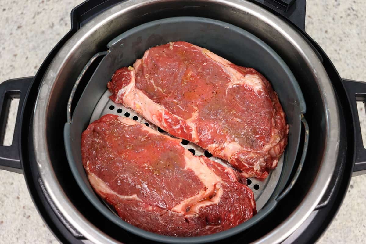Two uncooked ribeye rib fillet steaks in an air fryer