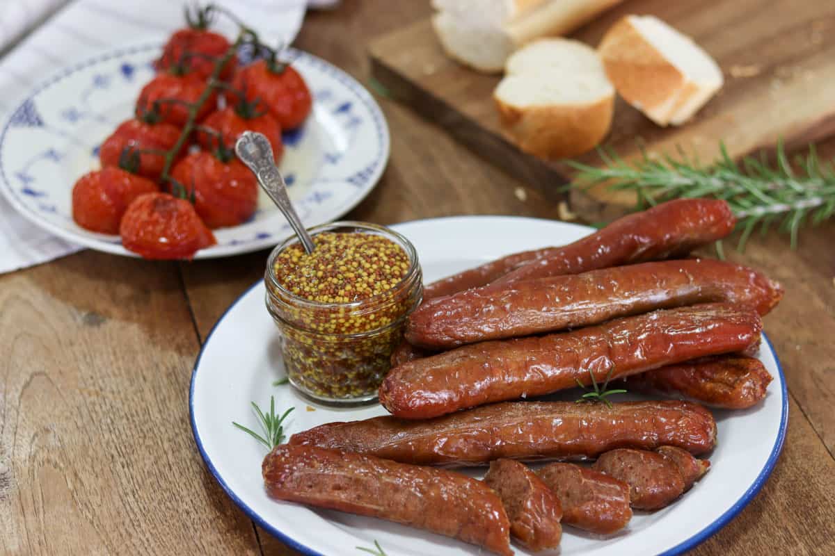 cooked sausages served on a plate with a jar of mustard